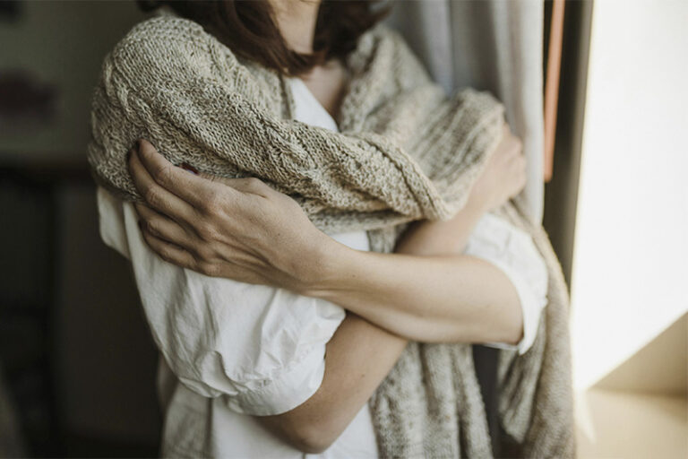 Woman with a sweater on her shoulders snuggling up, represents how Grief Counseling in Orange County can help honor your loss while moving forward.