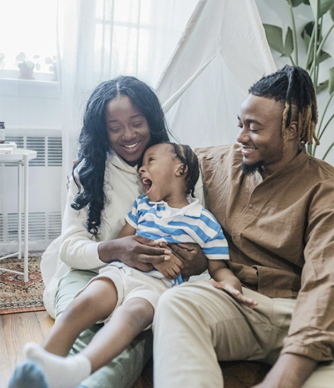 Boy sitting on his parents lap and laughing, represents how working with marriage and family therapist in Orange County can help you feel stronger and happier.