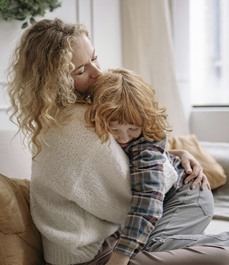 Mother hugging her son while sitting in the couch, represents how parenting therapy can help you feel less stress and more connection.