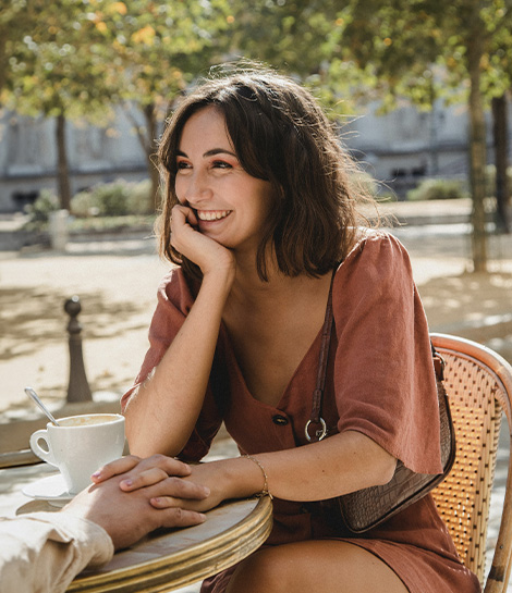 Woman smiling while holding hands in a outdoor cafe, represents how women's therapy can help you grow within yourself and in your relationships.
