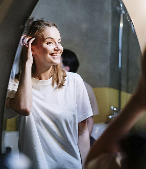 Woman smiling to herself in the mirror, represents how working with a women's therapist can help you feel more confident and happier.