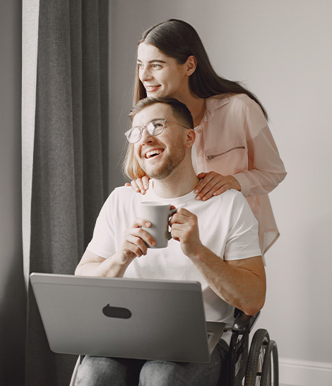 Happy couple, with the man in a wheelchair and a laptop on his lap, represents how online counseling in California can give you the comfort and flexibility you need.