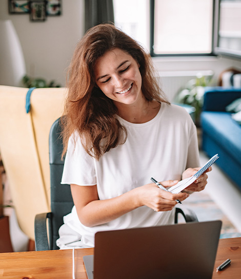 Woman at her laptop smiling while taking notes, represents how cognitive behavioral therapy can help you reframe your thoughts and feel better.